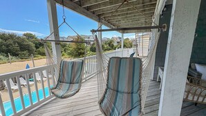 A wooden deck with two striped lounge chairs and a pool in the background. - DOLPHIN DUNES - 7 BR Oceanside Retreat In DUCK - Pool, Dogs allowed (Duck)