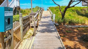 A wooden boardwalk leading to a beach with a sign instructing to clean up after dogs. - DOLPHIN DUNES - 7 BR Oceanside Retreat In DUCK - Pool, Dogs allowed (Duck)