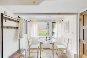 A dining area with a round table, four white chairs, a bench, and a view of a house through a window. - Cozy home with full kitchen, fast wifi & easy beach access (Seattle)