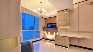 A modern hotel room with a large window, a flat-screen TV, a sofa, and a reception desk. - Maisón By SanLiving - 3BR - Kasablanka (Jakarta)