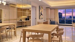 A modern dining area with a wooden table and chairs, a chandelier, and a large window with a city view. - Maisón By SanLiving - 3BR - Kasablanka (Jakarta)