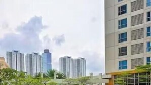 A swimming pool with clear blue water, surrounded by greenery and a tall building in the background. - Maisón By SanLiving - 3BR - Kasablanka (Jakarta)