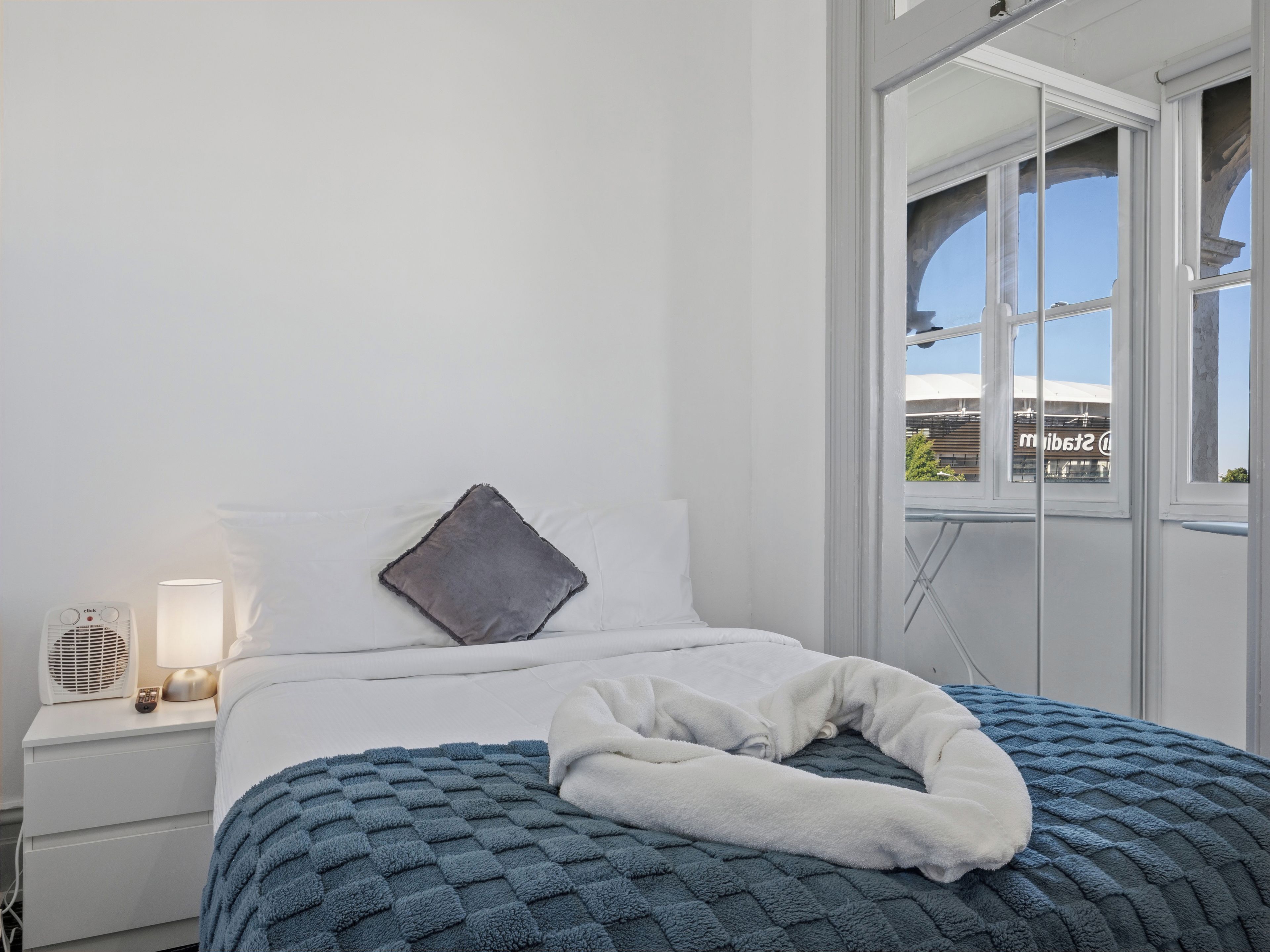 Una camera d'albergo con un letto, un comodino con una lampada e una finestra vista su un edificio.