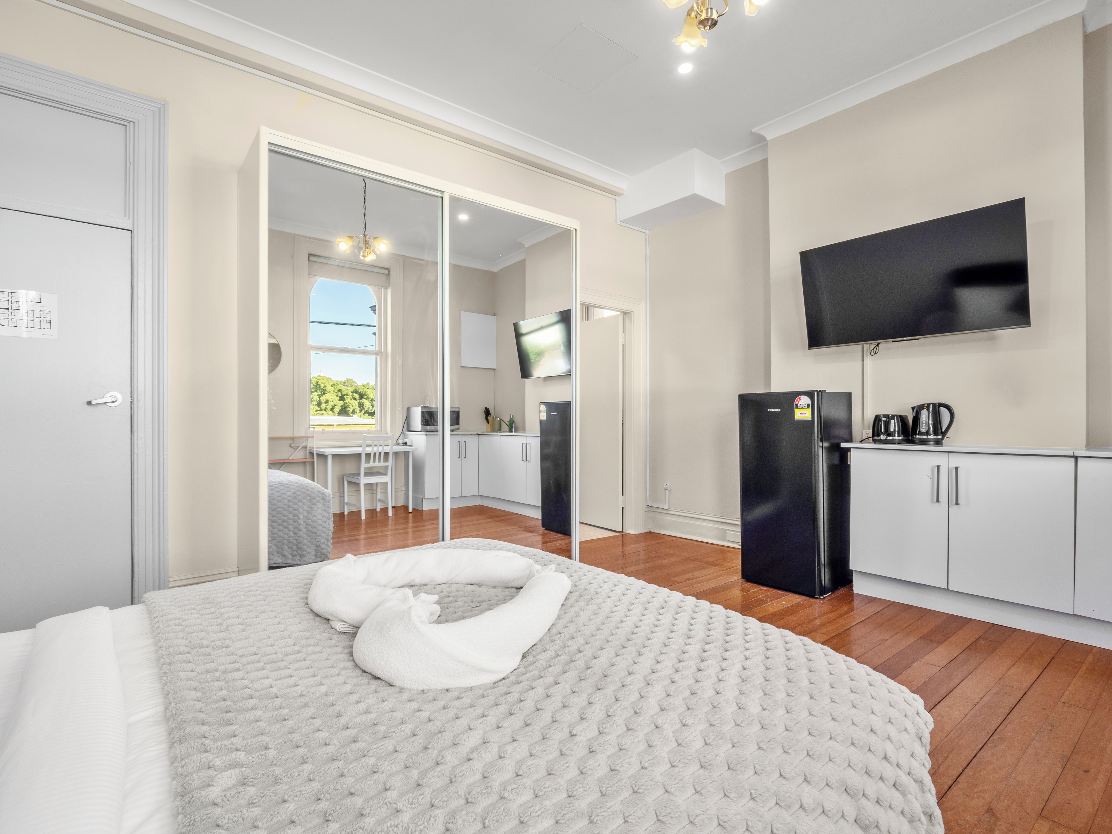 Quarto de hotel com cama, televisão, cozinha compacta e porta de correr para varanda.