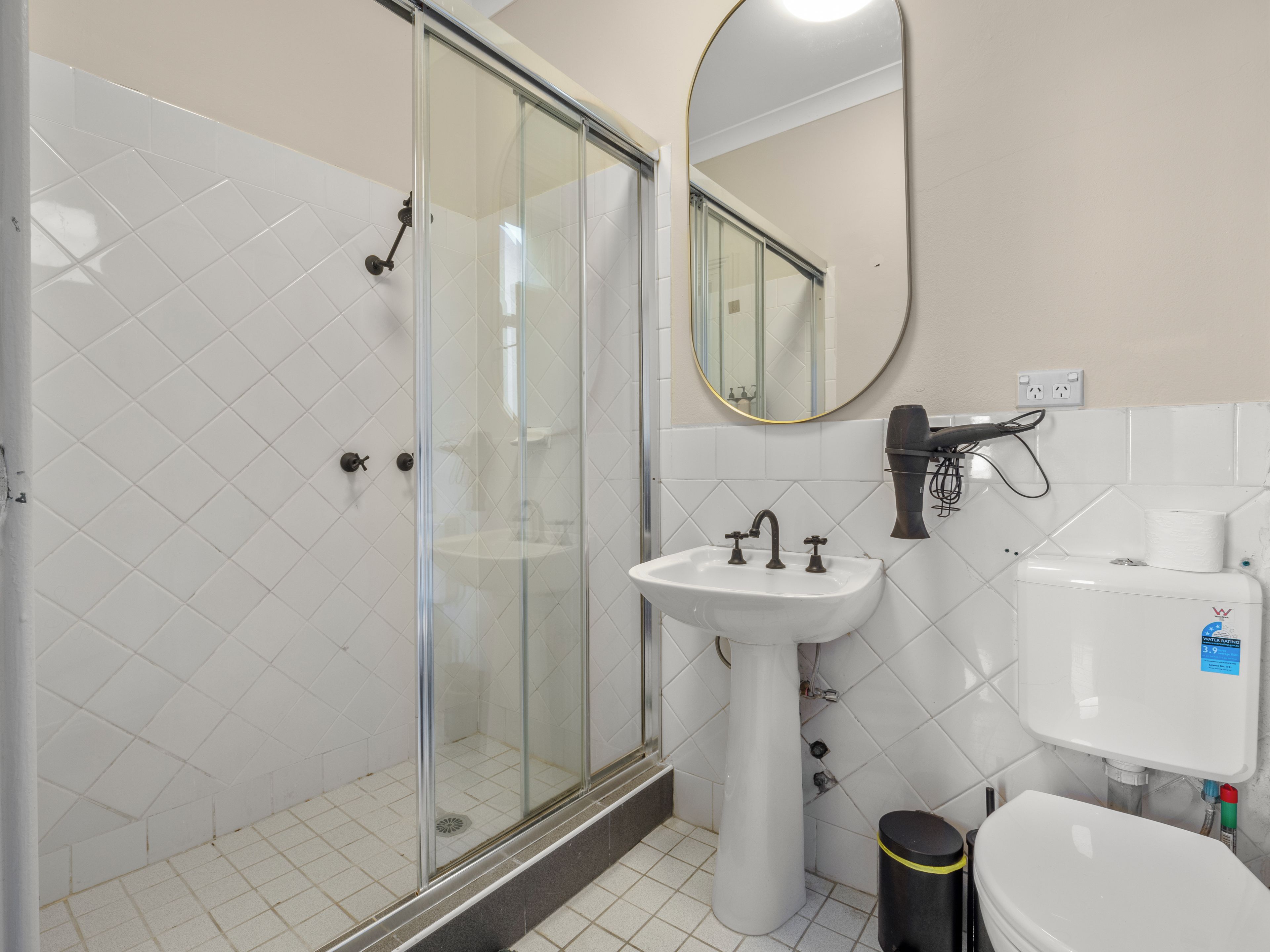 A bathroom with a glass-enclosed shower, a pedestal sink, a toilet, and a mirror.