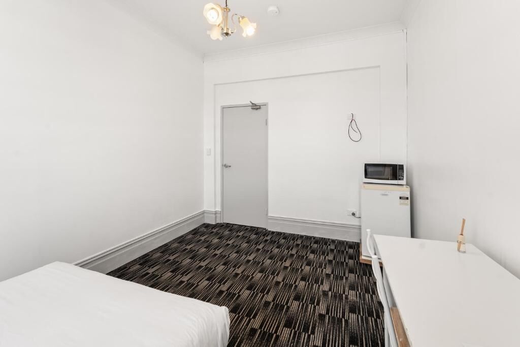A hotel room with a bed, a desk, a microwave, and a door.