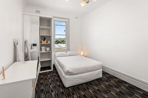 A bedroom with a bed, a white desk, a wardrobe, and a window with a view.