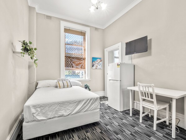 Une chambre avec un lit, un bureau, une chaise, un réfrigérateur, une fenêtre donnant sur un beau paysage et un téléviseur fixé au mur.