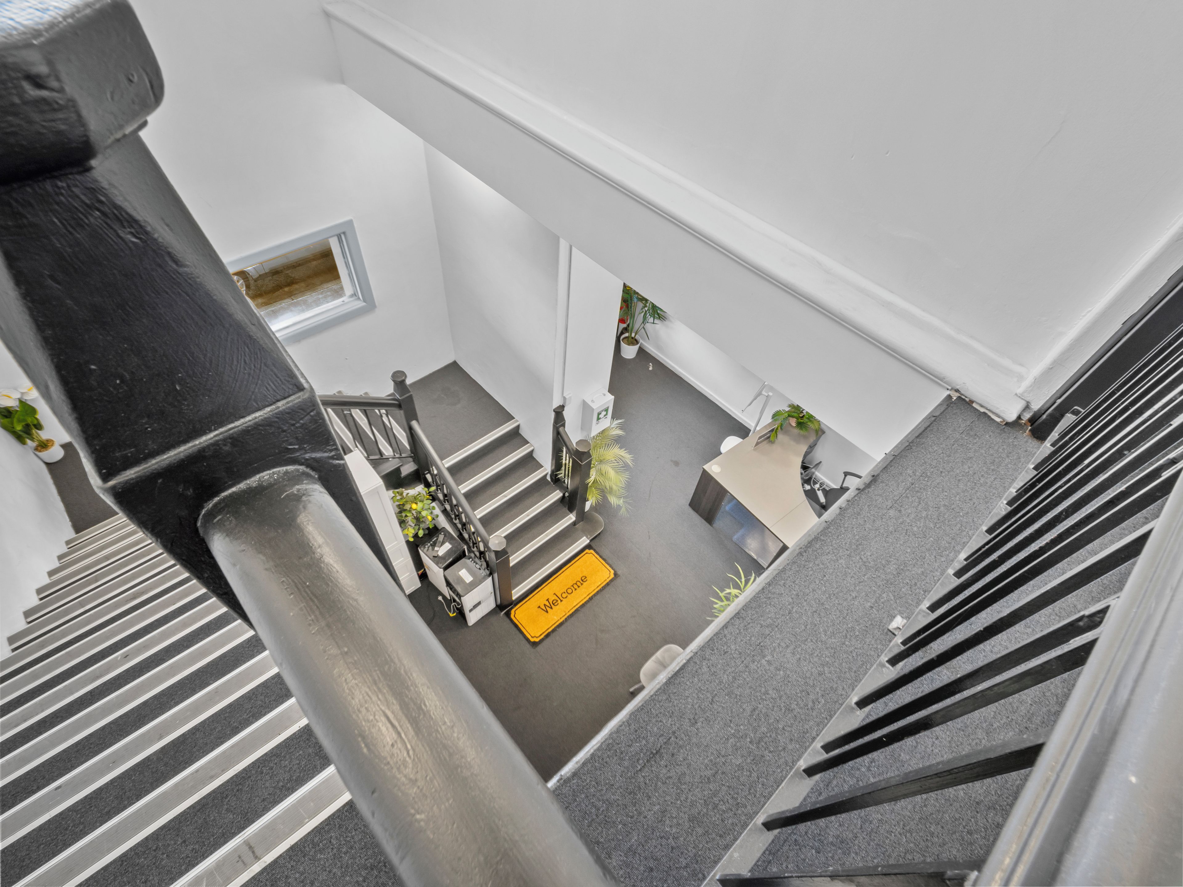 A view from a high floor looking down at a reception area with a 'Welcome' sign, a reception desk, and a staircase.