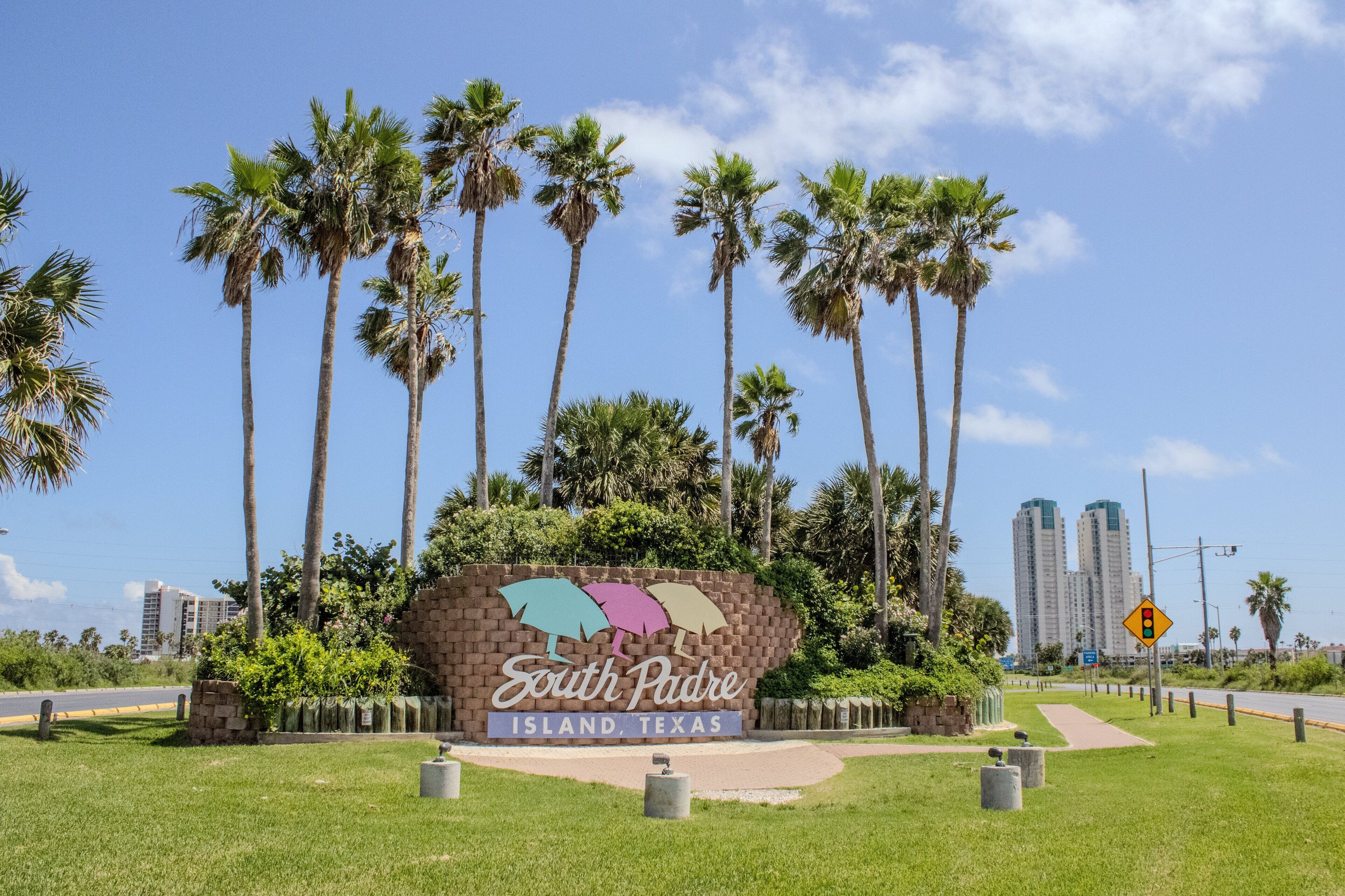 Letrero de South Padre Island, Texas, rodeado de palmeras y cielo despejado.