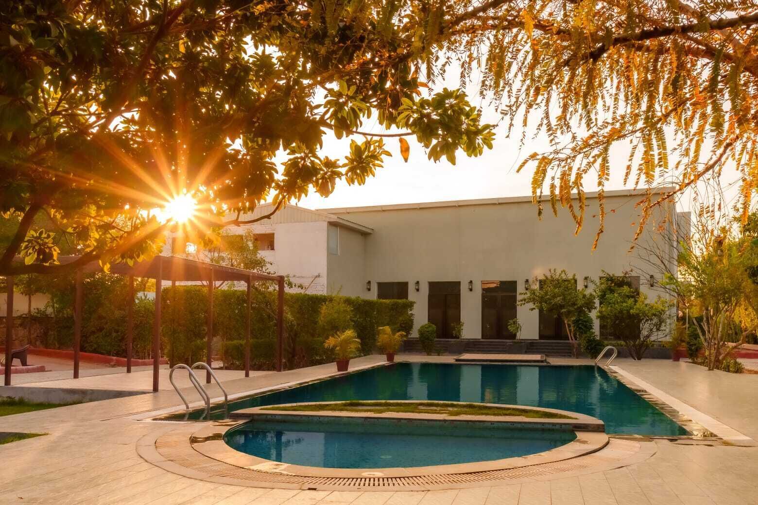 A swimming pool with a sunlit background, surrounded by a building with multiple doors and a covered walkway.