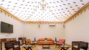 A living room with a patterned ceiling, a flat-screen TV, wooden furniture, and a sofa. - Aureva Raj Bagh Retreat (Jaipur)