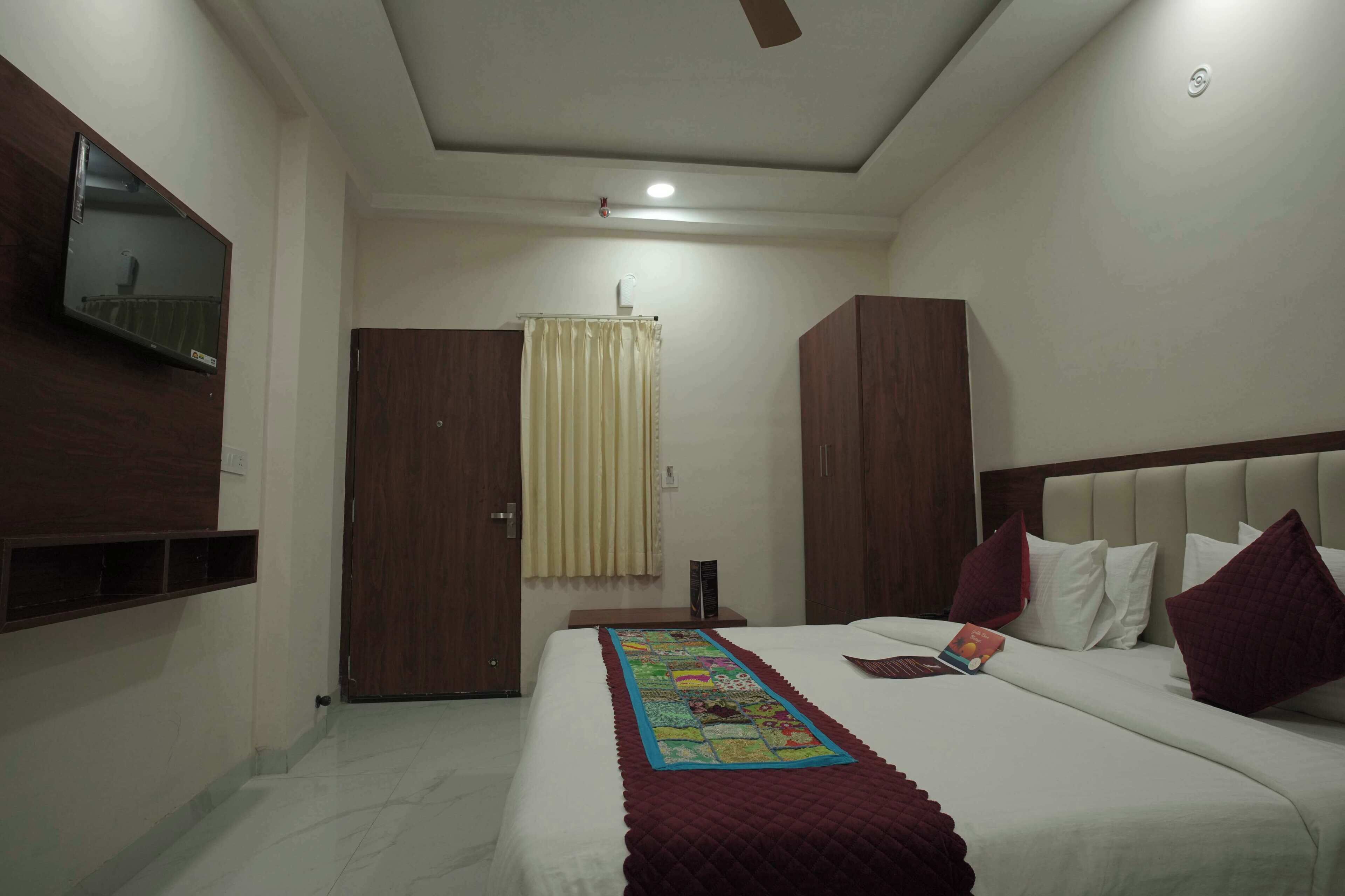 A hotel room with a bed, a TV mounted on the wall, a ceiling fan, and a window with curtains.