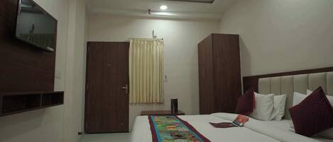 A hotel room with a bed, a TV mounted on the wall, a ceiling fan, and a window with curtains.