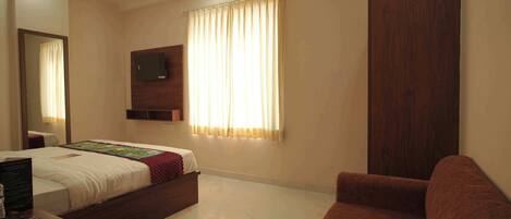 A bedroom with a bed, a TV mounted on the wall, a ceiling fan, a window with curtains, and a wooden wardrobe.