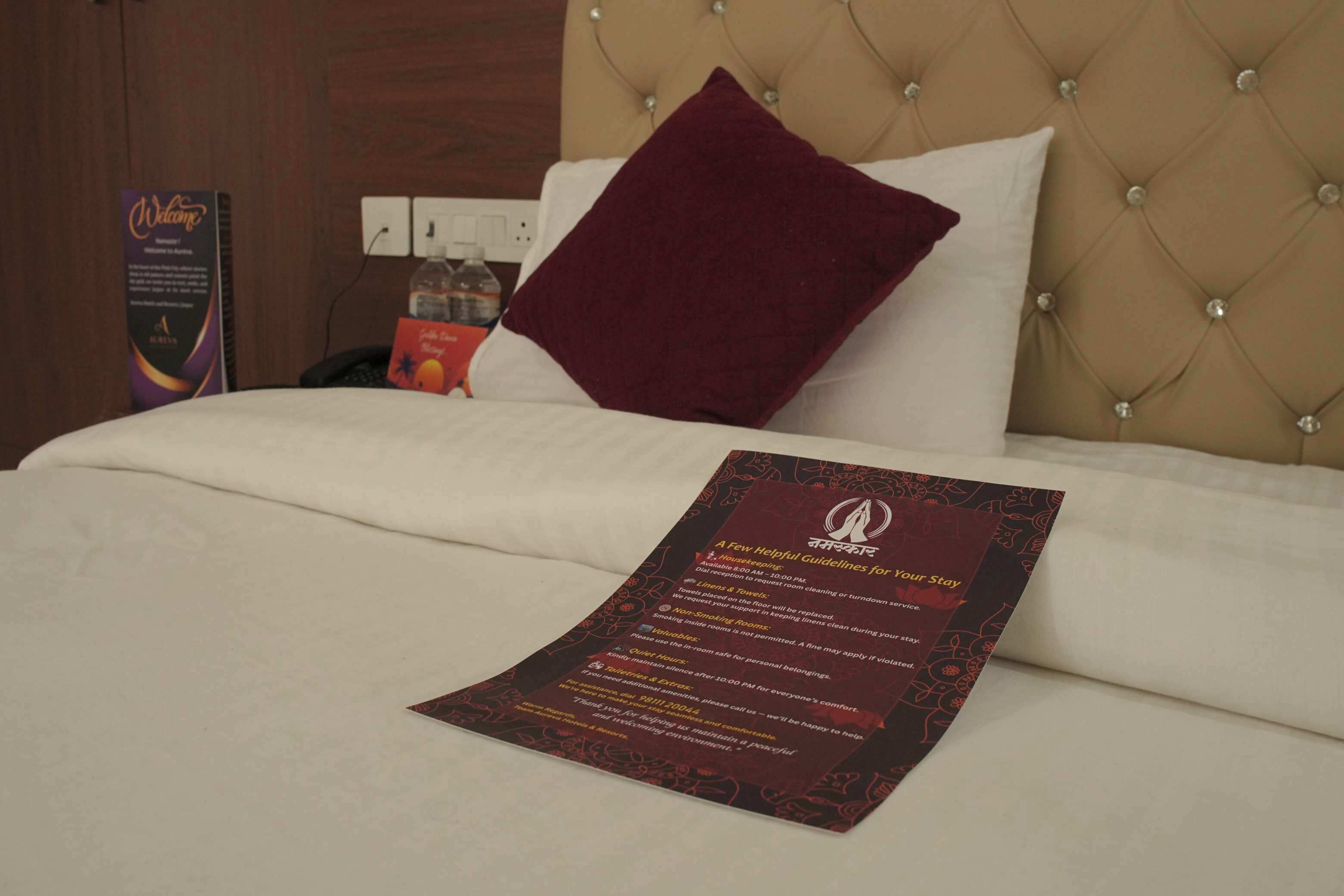 A hotel room with a neatly made bed, a welcome sign, and a printed guideline for guests.