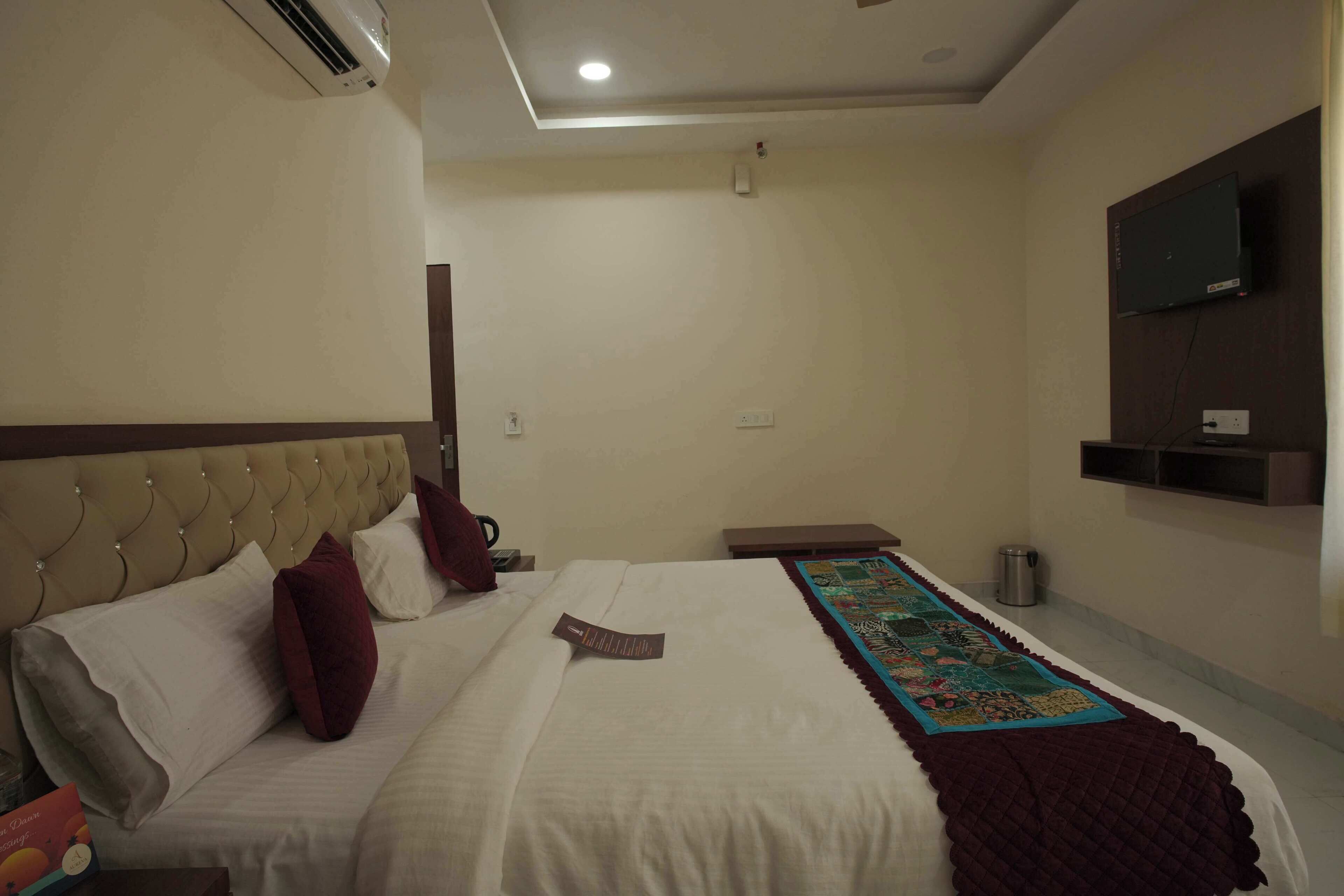 A hotel room with a bed, a TV mounted on the wall, and a small table.