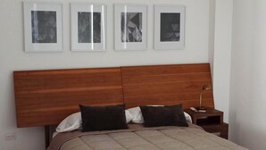 A bedroom with a wooden headboard, a bed with a beige duvet, and three framed pictures on the wall.