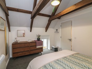 A bedroom with a wooden dresser, a bed with a patterned bedspread, a potted plant, a mirror, and a door with a hanger. - THE LOFT, family friendly, with a garden in Glenmore, County Kilkenny (Kilkenny)