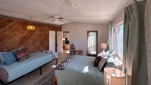 A bedroom with two beds, a ceiling fan, a window with curtains, and a door leading to another room. - Desert Serenity Private Patio Mountain View 1BR (Tucson)