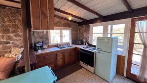 A rustic kitchen with stone walls, wooden beams, a gas stove, a vintage refrigerator, and a window with curtains. - Desert Serenity Private Patio Mountain View 1BR (Tucson)