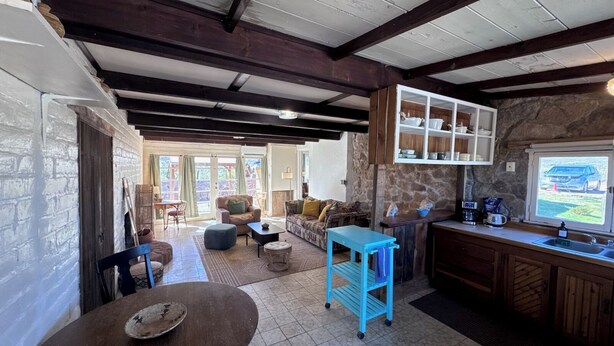 A rustic interior with a stone wall, wooden beams, a kitchen with a stone countertop, and a view of a vehicle outside. - Desert Serenity Private Patio Mountain View 1BR (Tucson)