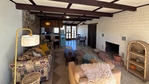 A cozy living room with a fireplace, a patterned sofa, and a dining area with a kitchen in the background. - Desert Serenity Private Patio Mountain View 1BR (Tucson)