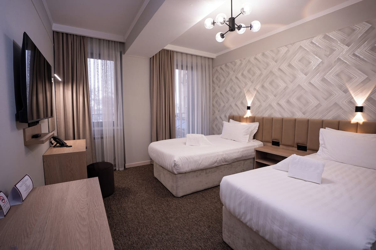 A hotel room with two beds, a desk, a TV, and a patterned wall.