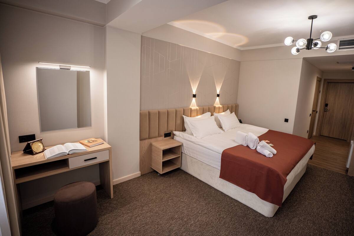 A hotel room with a bed, bedside table, desk, chair, and a mirror.