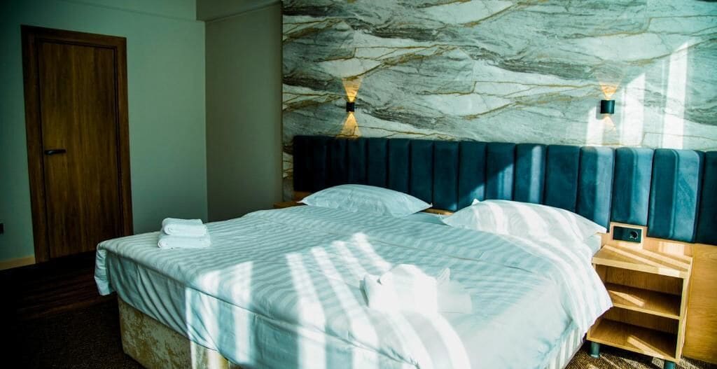 A hotel room with a bed, a wooden nightstand, and a marble-patterned headboard.