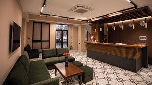 A modern lobby with a reception desk, green sofas, a patterned floor, and a vase of flowers on a table. - Hotel Orto Asia (Bishkek)