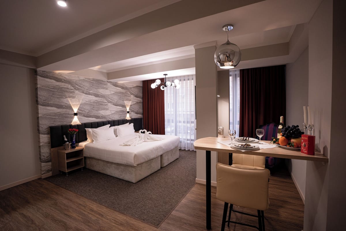 A modern hotel room with a large bed, a dining table, and a seating area.