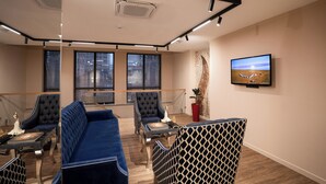 A modern room with a blue sofa, two armchairs, a small table, and a TV on the wall. - Hotel Orto Asia (Bishkek)