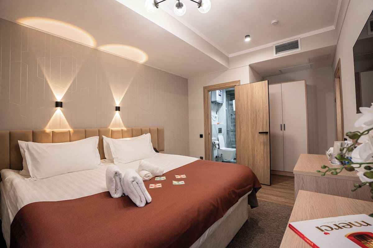A hotel room with a large bed, a wooden headboard, and a bedside table with a book.