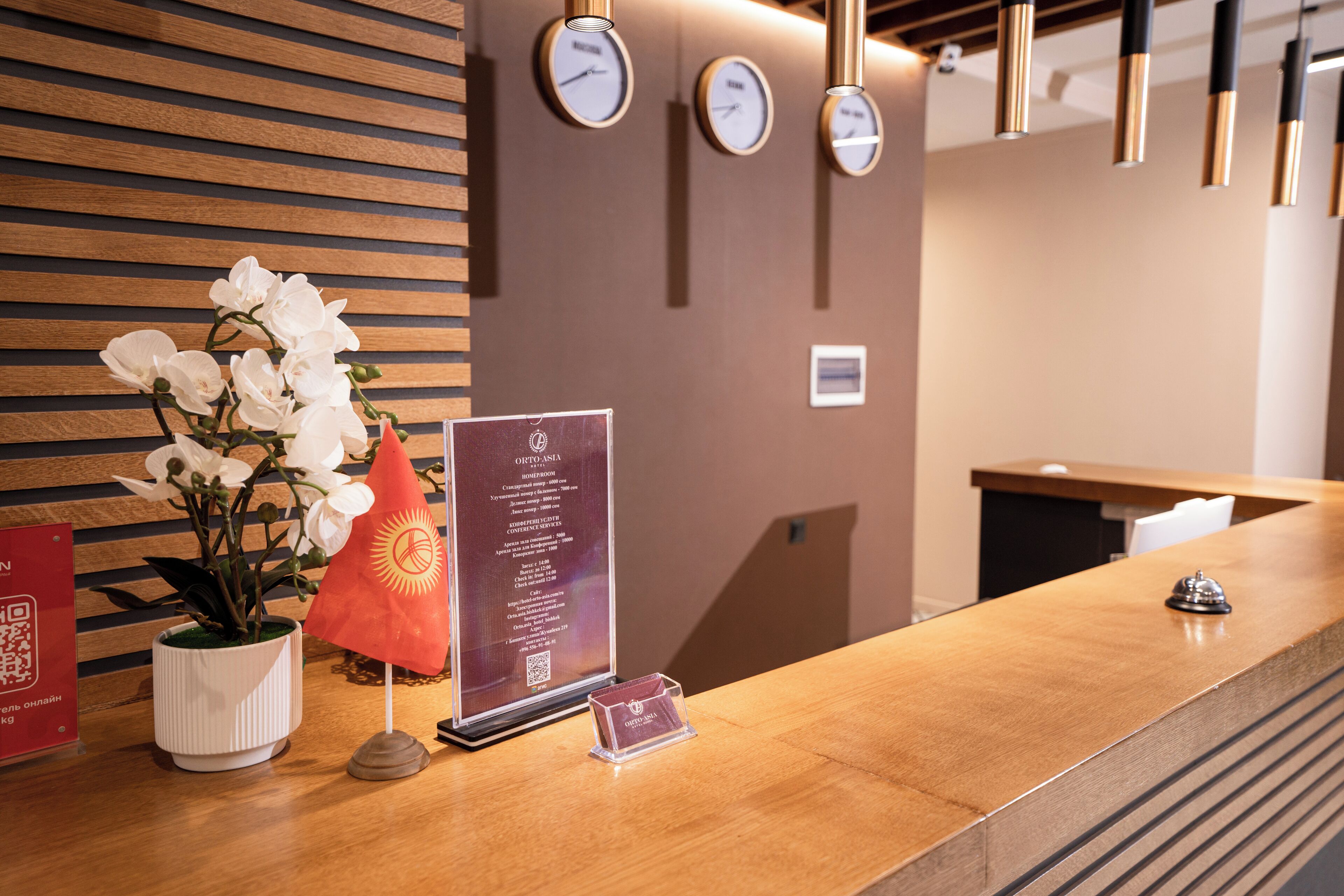 A reception desk with a wooden finish, a potted white orchid, a red flag, and a QR code sign.