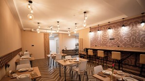 A hotel dining area with multiple tables set for dining, a bar area, and a patterned wall in the background. - Hotel Orto Asia (Bishkek)