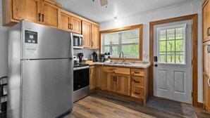 Eine Küche mit Holzschränken, einem Edelstahlkühlschrank, einer Mikrowelle und einem Fenster mit Jalousien.