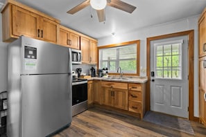 A kitchen with wooden cabinets, a stainless steel refrigerator, a microwave, and a window with blinds.