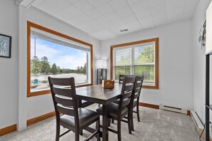 A dining area with a table and chairs, large windows with blinds, and a view of a lake.