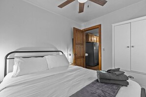 Un dormitorio con cama, armario, puerta que da a una cocina y ventilador de techo.