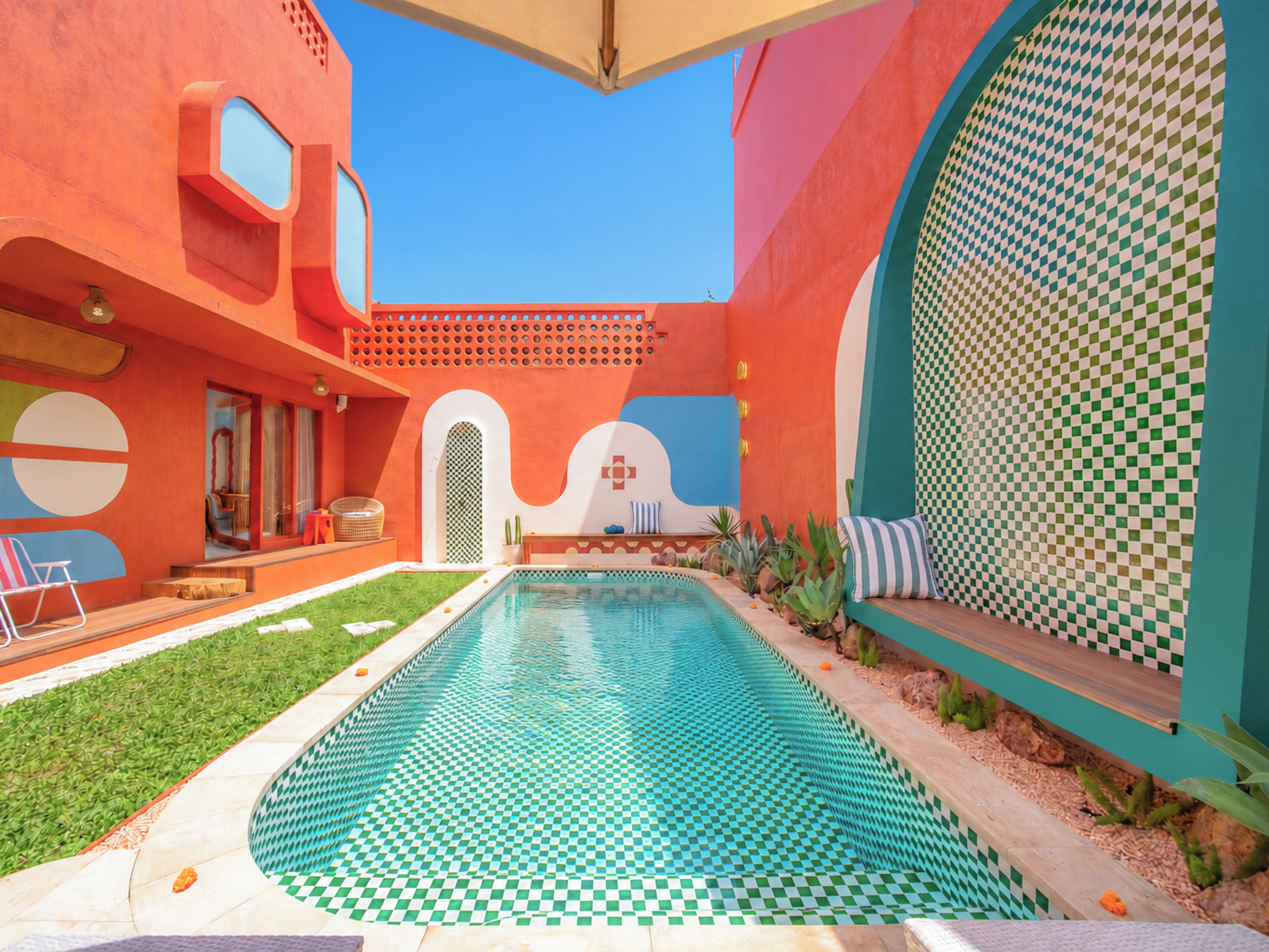 A pool area with a checkered floor, surrounded by a building with geometric patterns and a clear blue sky.