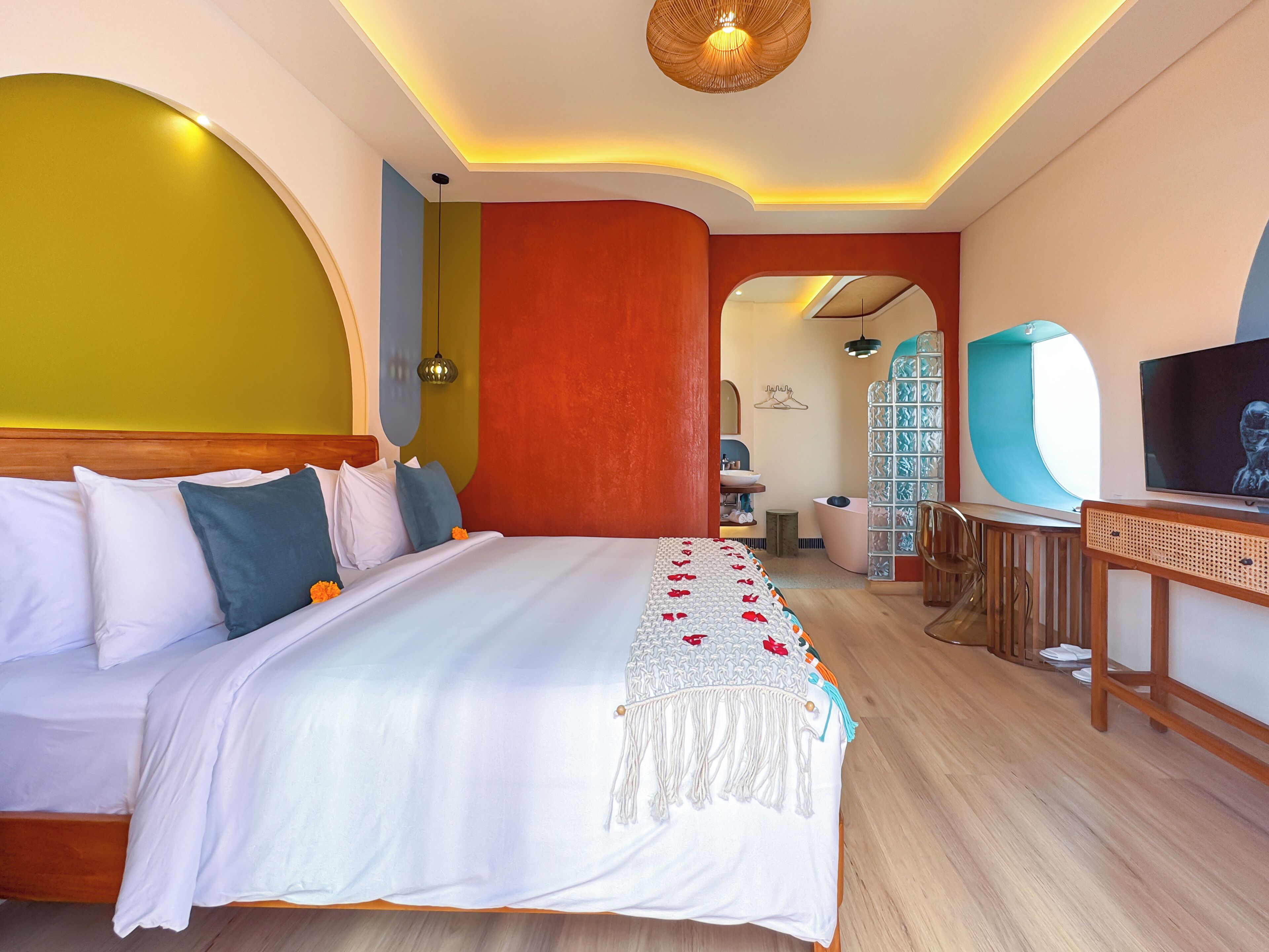 A modern hotel room with a large bed, a television, and a bathroom visible through an archway.