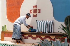 A person arranging cushions on a bench with a geometric wall design in the background. - Kana Casa Canggu by Nagisa Bali (Canggu)