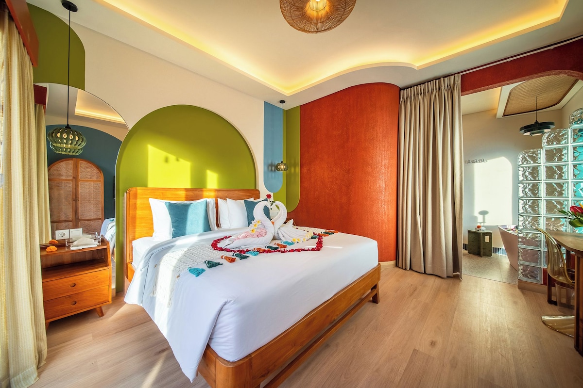 A hotel room with a large bed, a wooden headboard, a bedside table, and a mirror.