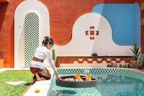A pool area with a decorative edge, a person tending to a water feature, and a wall with a geometric pattern. - Kana Casa Canggu by Nagisa Bali (Canggu)