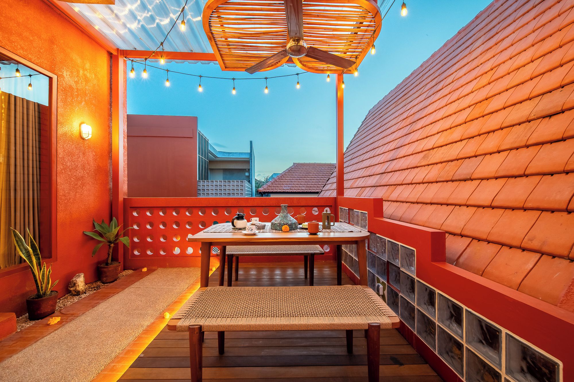 An outdoor seating area with a table and chairs, a ceiling fan, string lights, and a view of buildings in the background.