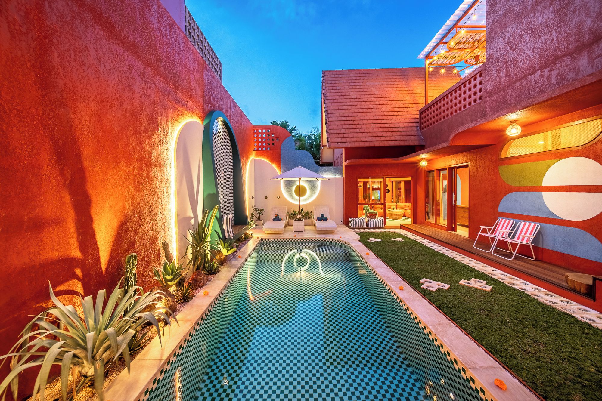A modern pool area with a checkered pattern, surrounded by walls with circular windows and a small garden with plants.