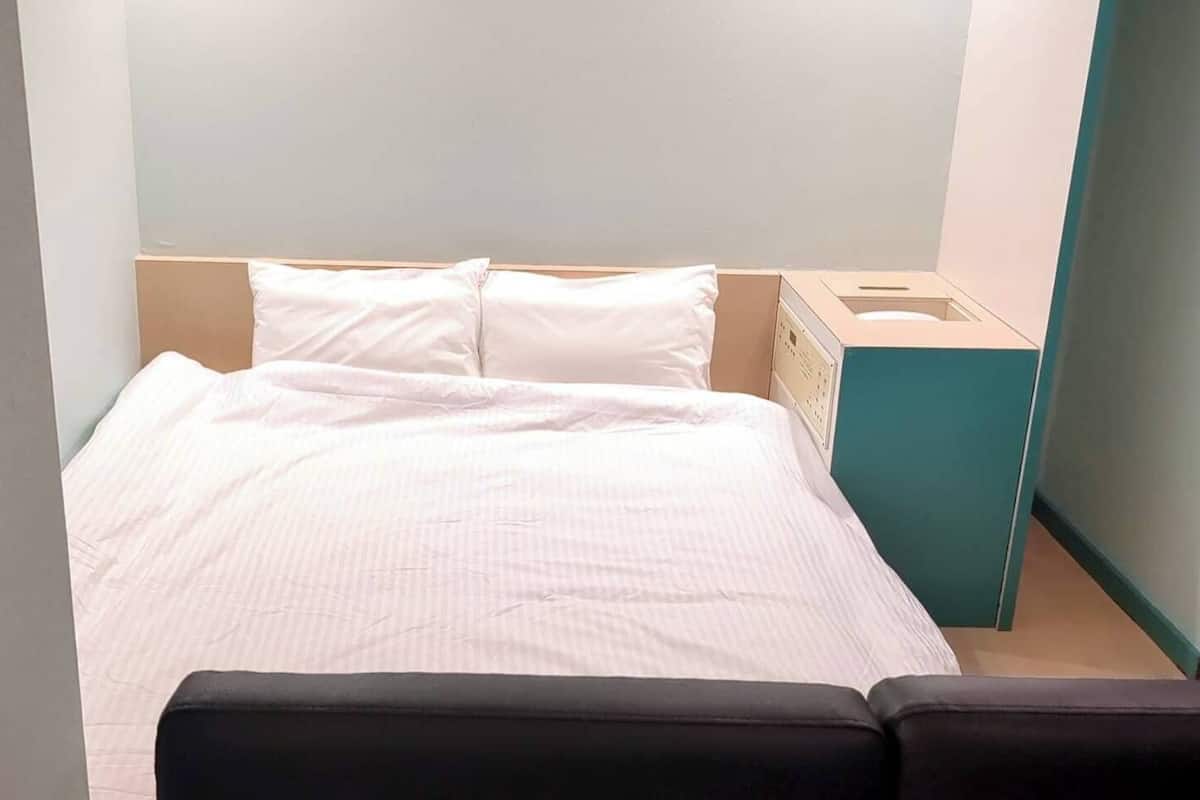 Un lit avec une literie blanche, une tête de lit et une table de chevet sur laquelle se trouve une boîte de mouchoirs.
