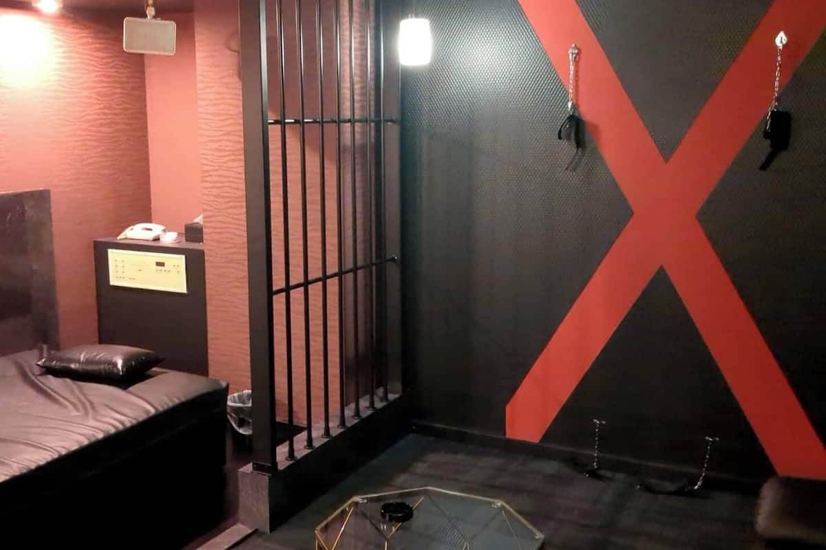 Une petite pièce faiblement éclairée, avec un lit, un bureau et un grand miroir.