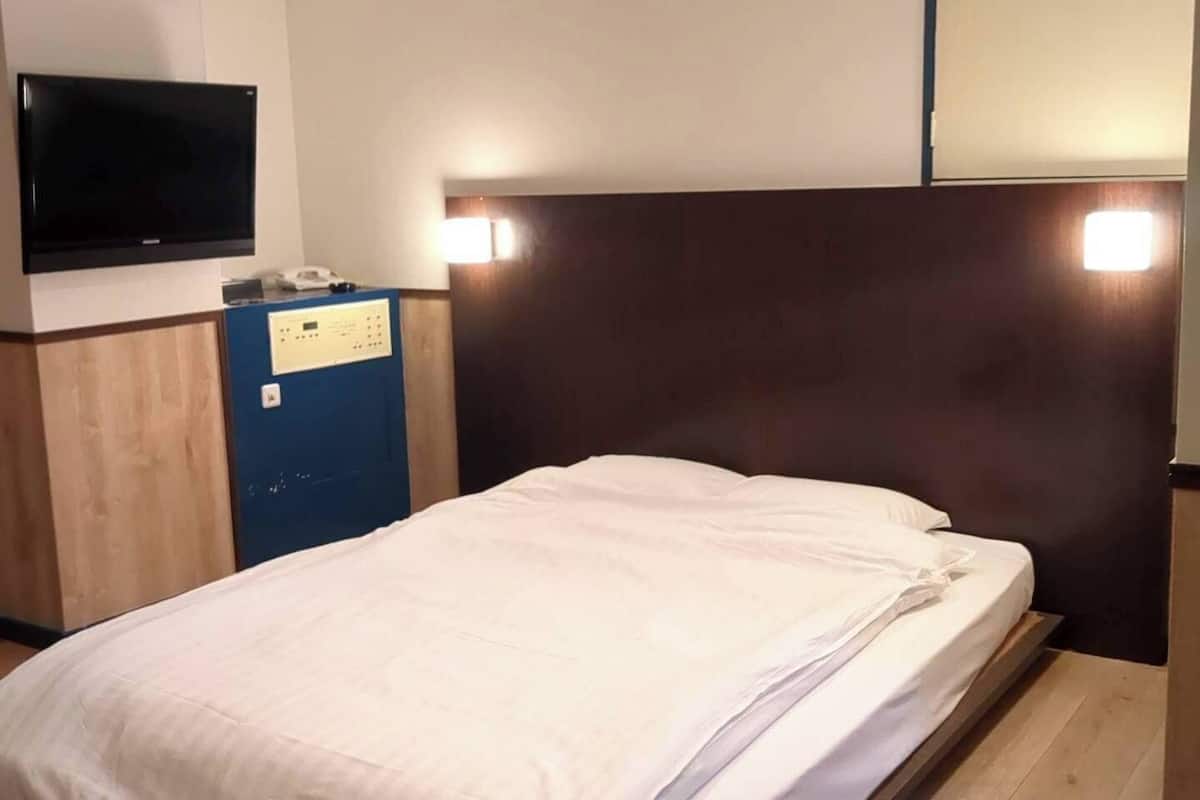 Une chambre d’hôtel équipée d’un lit, d’un bureau avec un téléphone et d’un téléviseur à écran plat fixé au mur.